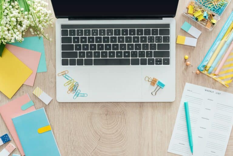 top view of laptop, stationery, notepads and pens on wooden table