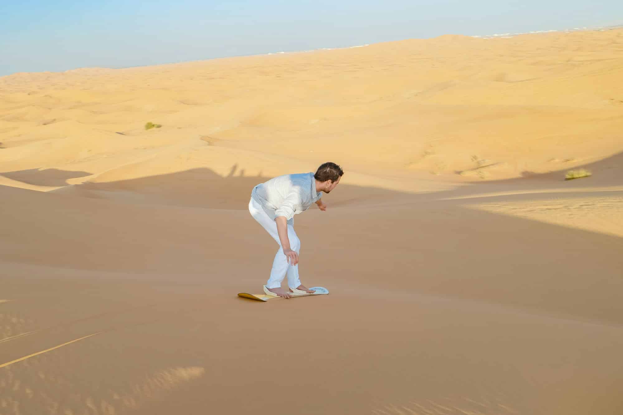 Young men sand surfing at the sand dunes of Dubai United Arab Emirates